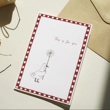 Load image into Gallery viewer, A square greeting card with a red-and-white checkered border and a simple illustration of a bird holding a flower, placed beside a kraft envelope on a light surface. Two small wrapped gift boxes with twine are visible in the background.
